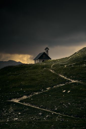 A vertical shot of a small house in a field on a cloudy sky background