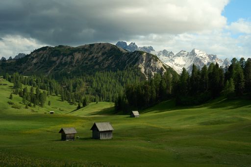 A scenic view of wooden huts in a green field on a mountainous background