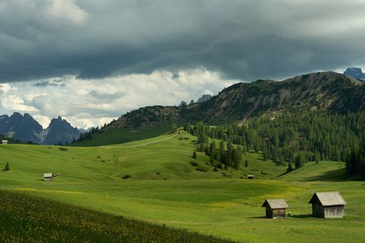 A scenic view of wooden huts in a green field on a mountainous background