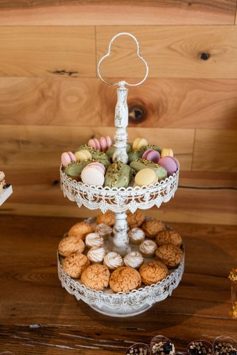 A vintage two-tiered dessert stand with assorted macarons and pastries displayed elegantly on a wooden table.