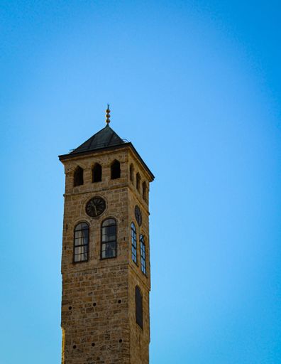 A historic clock tower with intricate architecture against a clear blue sky in Sarajevo, Bosnia and Herzegovina.