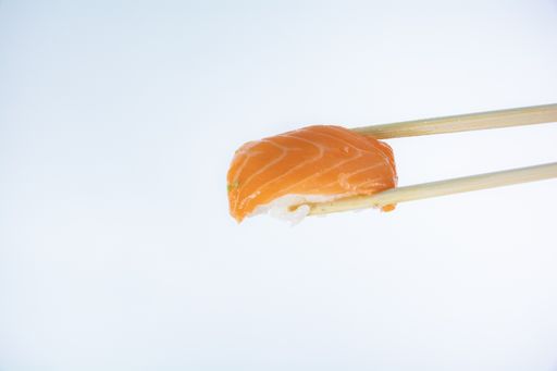 A closeup of salmon nigiri held with bamboo chopsticks isolated on white background with free space for test