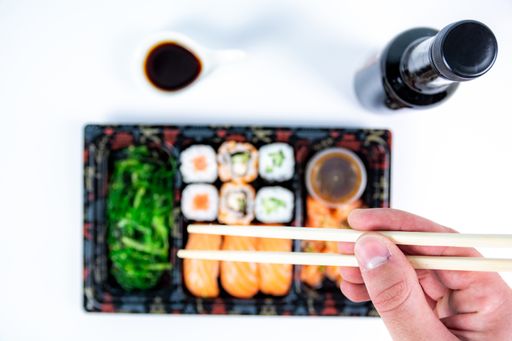 A hand holding chopsticks over the delicious sushi rolls on a tray