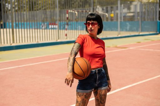 A portrait of a sexy confident Spanish woman with tattoos holding a ball at the basketball court