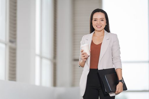 A happy successful Asian businesswoman holding a takeaway coffee cup and a digital tablet