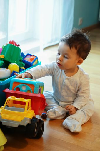 A vertical shot of an adorable baby boy sitting on the floor playing with colorful toys