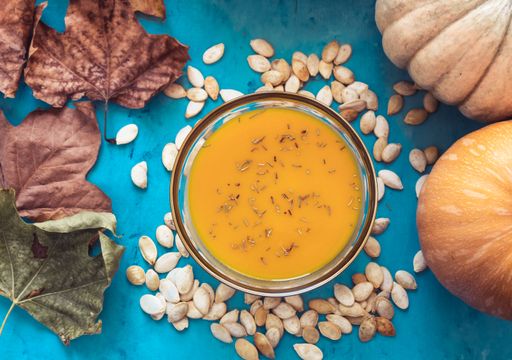 A top view of pumpkin soup with pumpkins, seeds, and dry Autumn leaves on the blue table