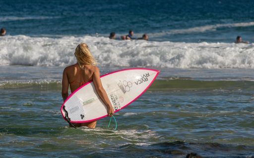 A female holding a surfboard entering into the ocean
