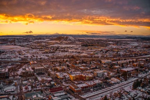Aerial view of a snowy cityscape at sunset with vibrant orange skies and distant mountains.