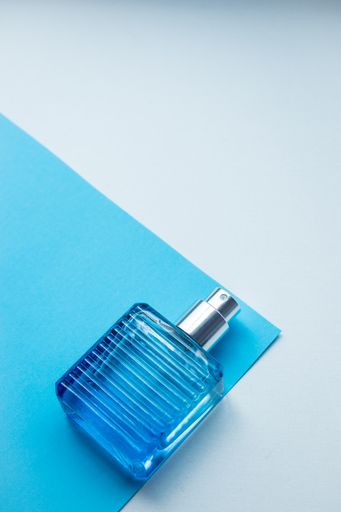 A vertical closeup of a blue perfume bottle on a blue and white background