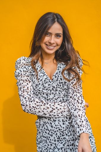 A vertical shot of a smiling woman wearing a dress on a yellow background
