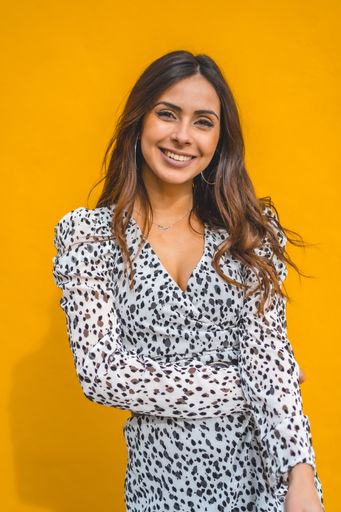 A vertical shot of a smiling woman wearing a dress on a yellow background