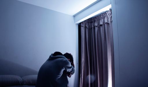 A horizon shot of a man sitting on bed and he look sad and depressed in his dark room