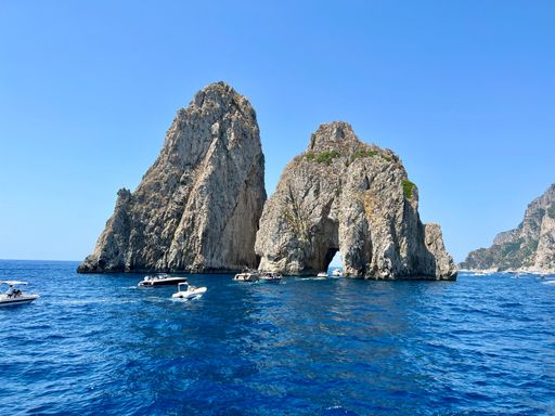 Scenic view of Faraglioni rocks in Capri, Italy, with boats on the vibrant blue Mediterranean Sea under a clear sky.