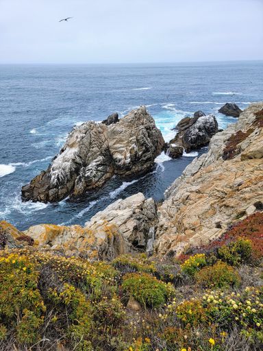 A vertical shot of rocks and cliffs surrounded by the sea under a cloudy sky