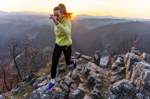 Young woman in sportswear jogging on rocky mountain trail at sunset with scenic view.