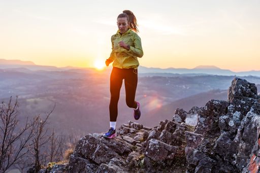 A young woman running on rocky terrain during a vibrant sunset, with mountains in the background.
