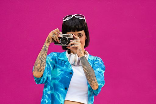A charismatic brunette young woman from Spain with tattoos posing with a vintage camera in a studio