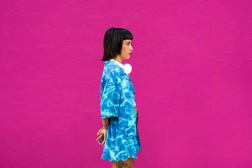 A side-view of a charismatic brunette young woman from Spain in a vibrant blue shirt in a pink studio