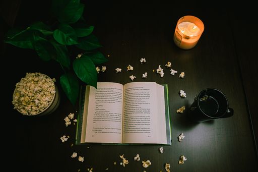 A high angle view of an open book and popcorn on the table with a lit candle and a cup of tea