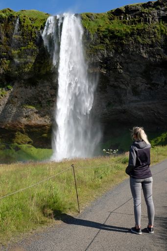 A vertical shot of a female in front of the Seljalandsfoss waterfall in southern Iceland
