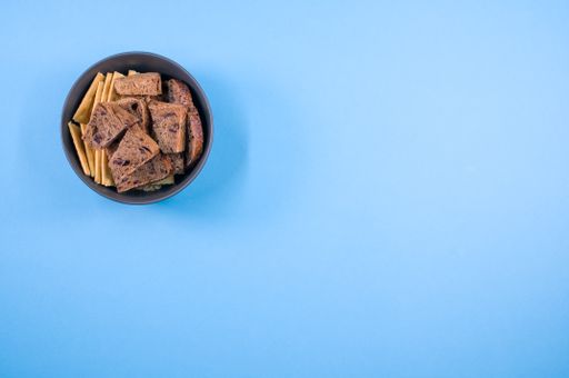 salty crackers with slices of organic brown bread in the bowl on a cyan background surface