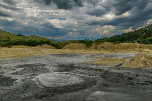 Dramatic landscape of muddy volcanoes under a cloudy sky in Romania, showcasing natural geological formations.