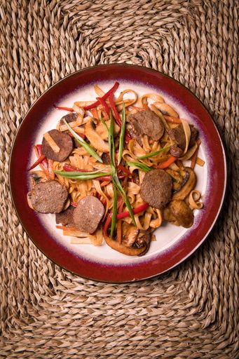 A top view of noodles with veal suki and vegetables on a weaving textu