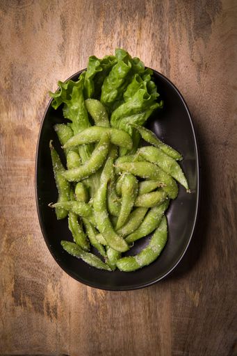 A top view of edamame beans and lettuce served on a black plate on a wooden surface