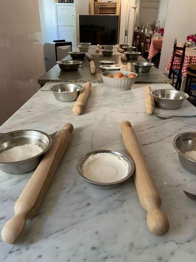 A kitchen setup with rolling pins, bowls of flour, and eggs on a marble countertop, ready for a baking class or cooking session.