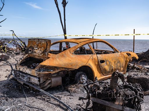 A rusted sportscar in a fire-damaged area, highlighting the aftermath of a wildfire