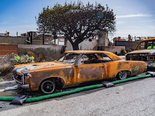 A rusted vintage car sits in a fire-damaged area, showcasing the impact of a recent blaze.
