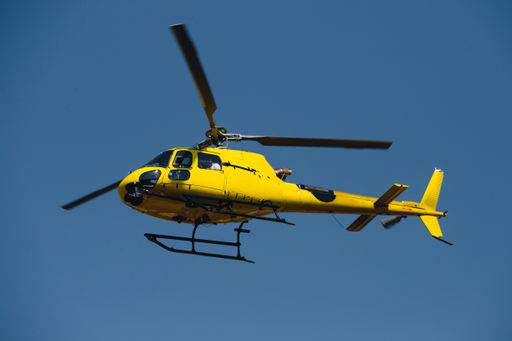 A closeup shot of a yellow helicopter flying in the clear skies