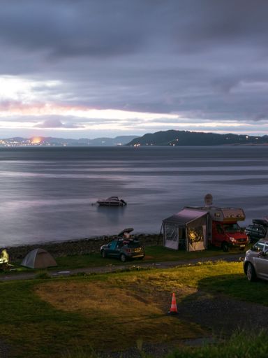 A sea under the night sky surrounded by mountains and a shore with camping cars and tents