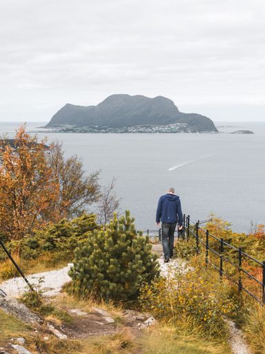 A scenic shot of a man going down a hill surrounded by a lake in Alesund, Norway