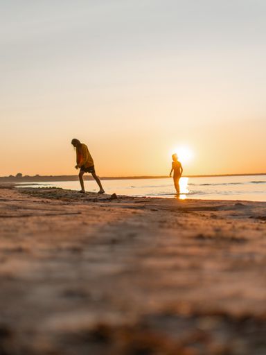 A scenic shot of two siblings playing around on the beach during the orange sunset