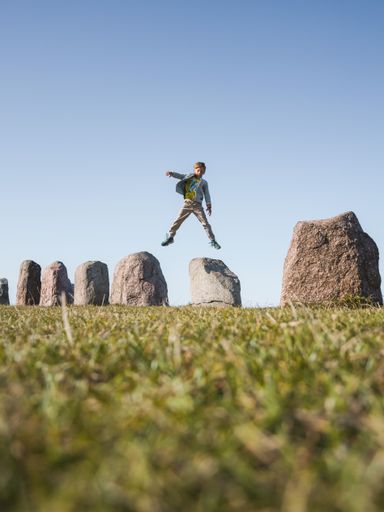 A beautiful shot of a Caucasian boy jumping off a rock in a field