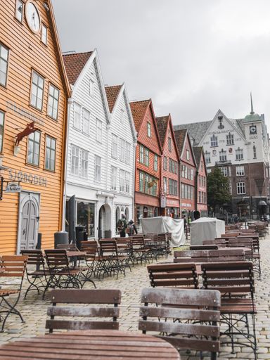 The old colorful buildings in Bergen, Norway with outdoor wood tables and chairs on a gloomy day