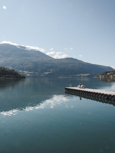 A scenic shot of a clear blue lake surrounded by mountain forests and a city