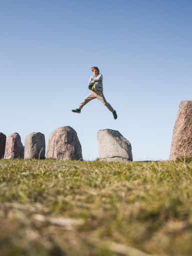 A beautiful shot of a Caucasian boy jumping off a rock in a field