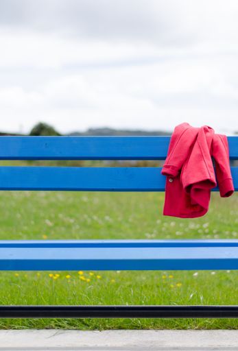 A closeup shot of a red jacket left on a blue bench