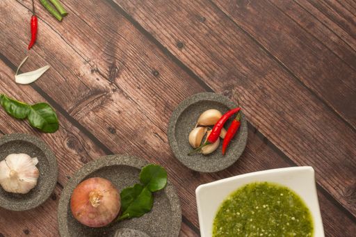 A top shot of garlic, onions, chili peppers, and green sauce in a white ceramic plate on a wooden table