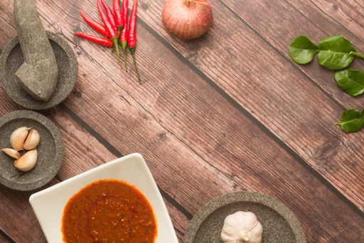 A top shot of garlic, onions, chili peppers, and red sauce in a white ceramic plate on a wooden table