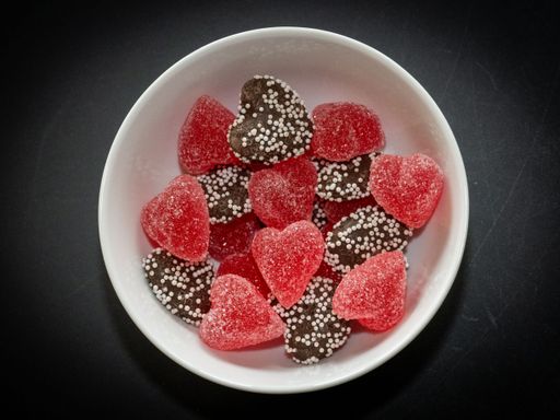 A bowl of heart-shaped gummy candies and chocolate hearts with sprinkles on a dark background