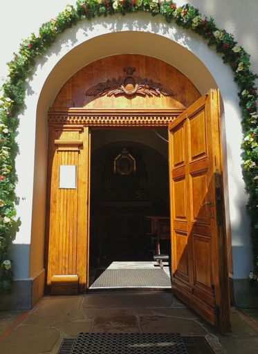 A vertical bright shot of an open arched wooden door leading to a church surrounded by flowers