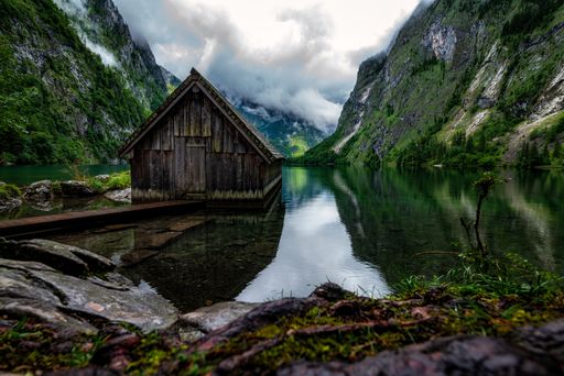 A scenic view of a wooden hut near the lake surrounded by mountains