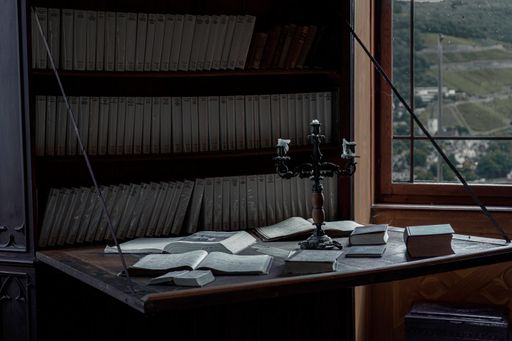 An eerie view of an antique bookcase, writing table with books, and a vintage candleholder