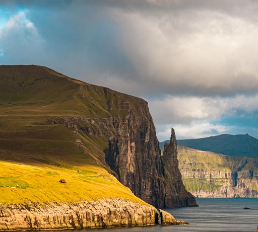 A beautiful scenery of rocky cliffs by the sea in the Faroe Islands under a cloudy sky