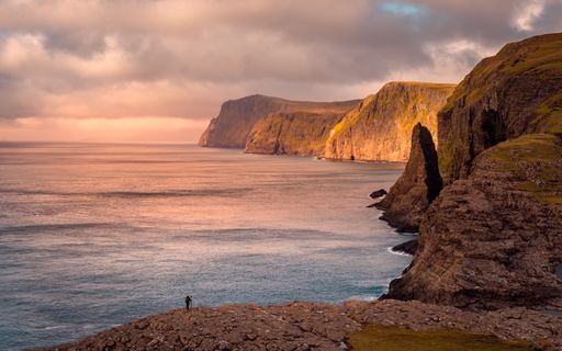 A beautiful scenery of rocky cliffs by the sea in the Faroe Islands under a cloudy sky