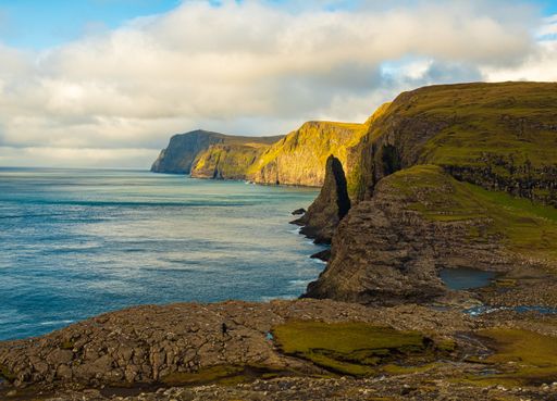 A beautiful scenery of rocky cliffs by the sea in the Faroe Islands under a cloudy sky